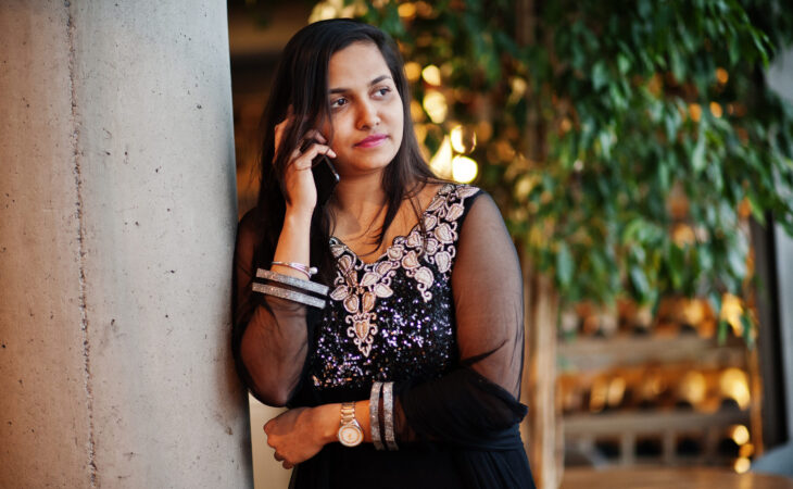 Pretty indian girl in black saree dress posed at restaurant with mobile phone at hand.